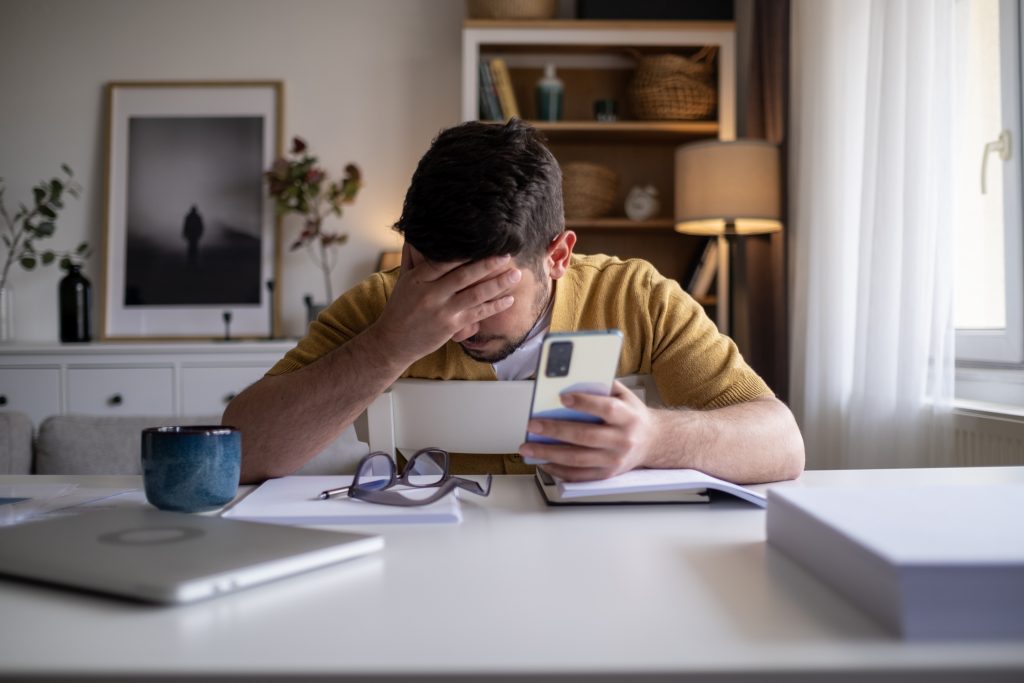 Shocked and surprised young businessman man sitting at desk in office and looking seriously at laptop monitor holding head.