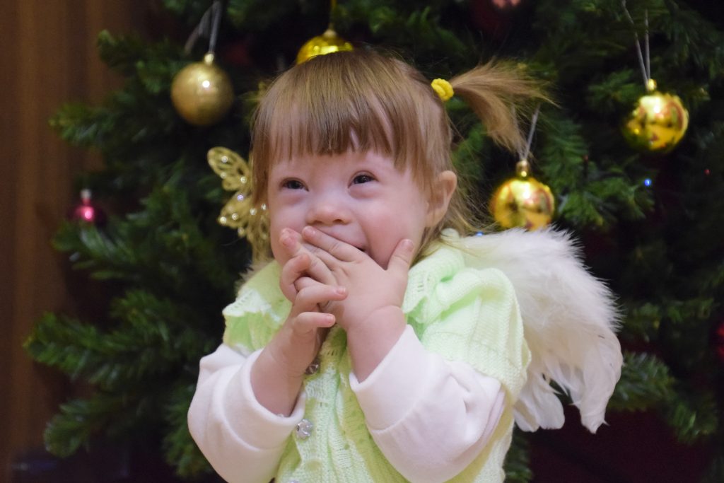 One year old baby girl sitting on the background of the Christmas tree. A child with gray eyes and blond hair.