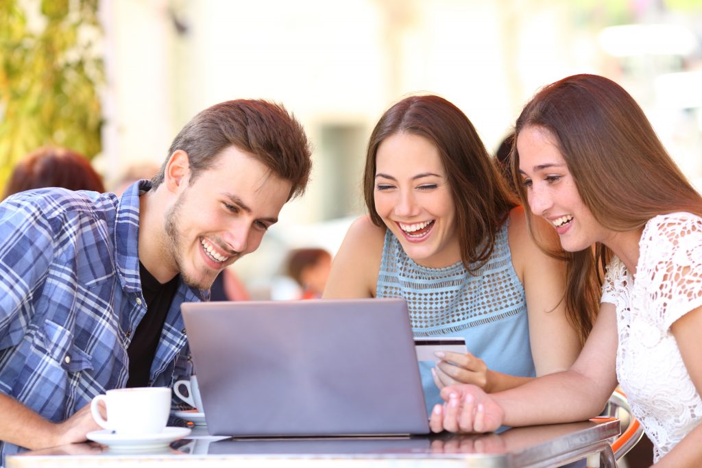 Happy shoppers paying online with credit card on a laptop in a coffee shop