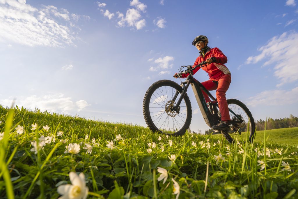 pretty mid age woman riding her electric mountain bike in early springtime in the Allgau mountains near Oberstaufen, in warm light with blooming spring flowers in the Foreground