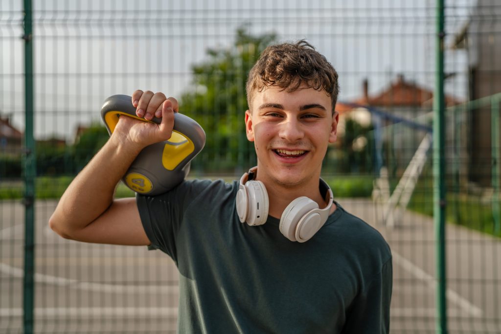 One man young caucasian male teenager stand outdoor in day training with russian bell girya kettlebell weight exercise real person copy space