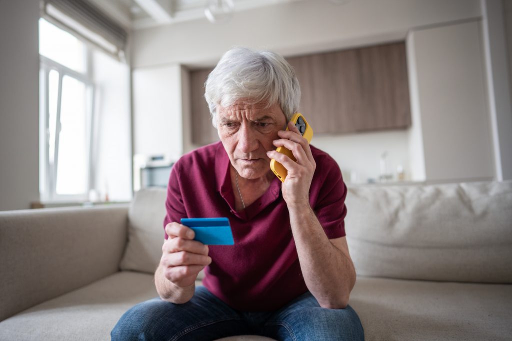 Naive elderly pensioner trusting sharing card number with scammers on phone. Identity theft, card fraud, manipulation, financial deception, personal data exposure, phone scam, dishonest schemes