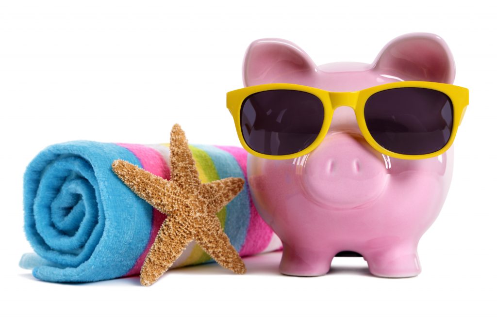 Pink piggy bank wearing yellow sunglasses on a beach with starfish and beach towel. Isolated on white.