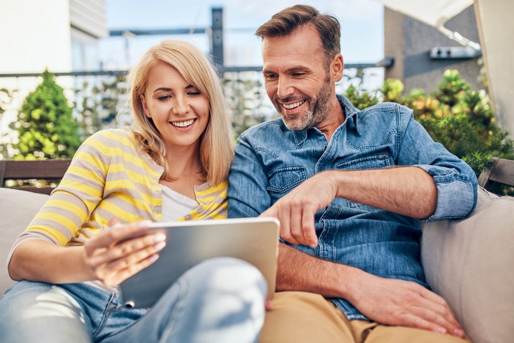 Adult couple using digital tablet at terrace sitting together on the sofa doing online shopping