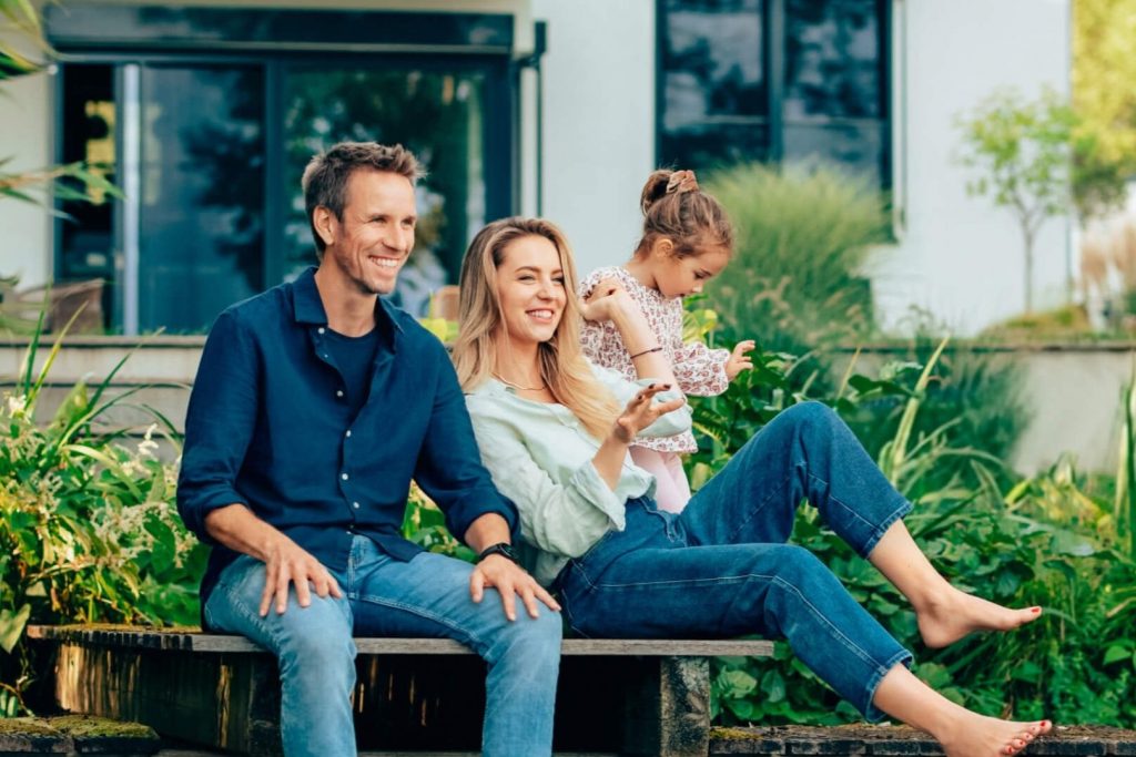 Eine Familie sitzt vor ihrem Eigenheim und lächelt.