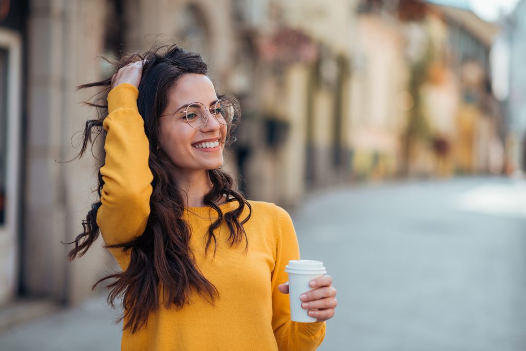 Gorgeous casual brunette in the town street, smiling and drinking coffee to go.