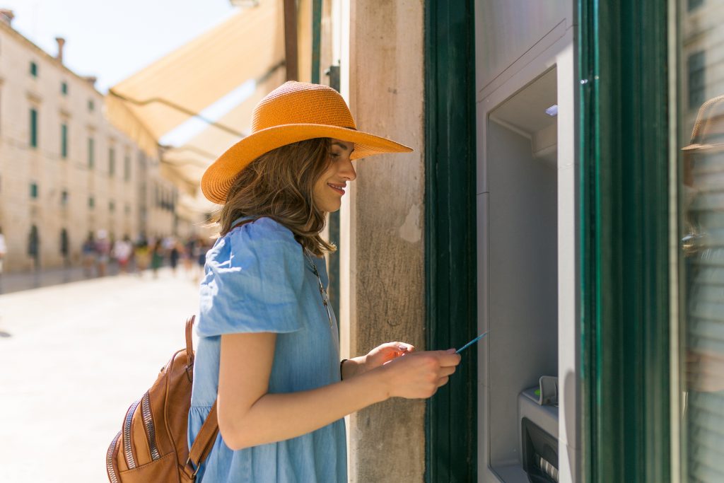 Beautiful girl taking the money from the ATM machine at her vacation.
