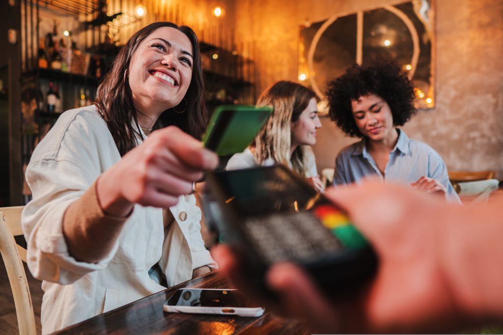 Happy young woman paying bill with a contactless credit card in a restaurant. Female smiling holding a creditcard and giving a payment transaction to the cashier. High quality photo